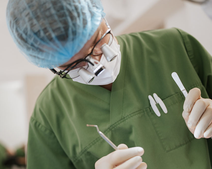 Dr Schipp trägt einen Mundschutz und eine Haube und führt eine Zahnoperation bei einem Patienten durch