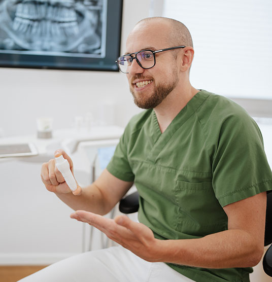 Dr Neubert hält ein Implantat aus Keramik in der Hand und berät einen Patienten