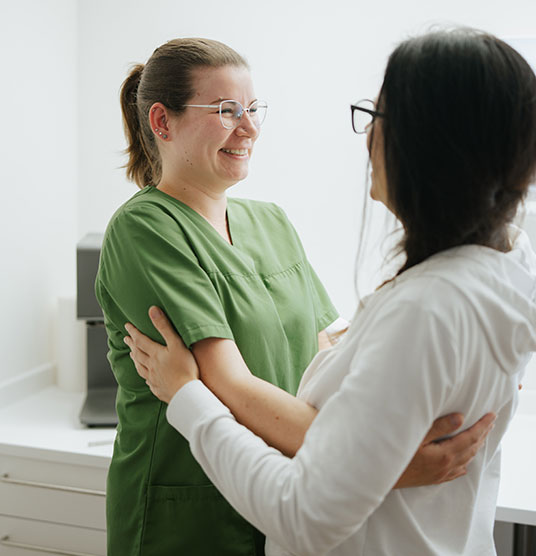 Seitenansicht, wie sich zwei Damen gegenseitig an den Armen halten und anlächeln