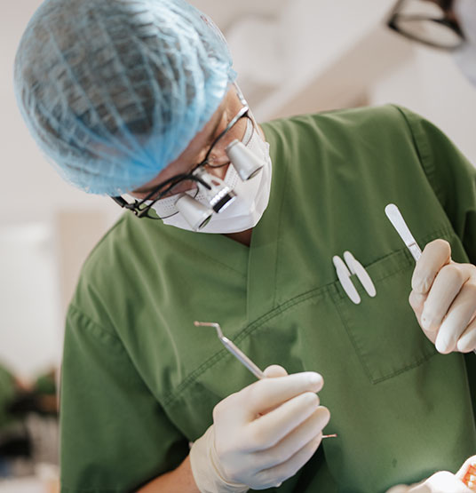 Dr Schipp führt eine Zahnoperation durch. Er trägt Mundschutz und eine blaue Haube